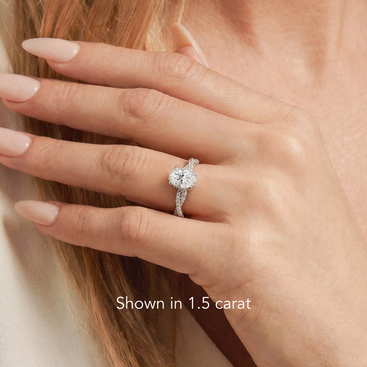 A close-up of a woman's hand wearing a heart-shaped diamond engagement ring on a silver band, with text overlay reading 'Shown in 1.5 carat'.