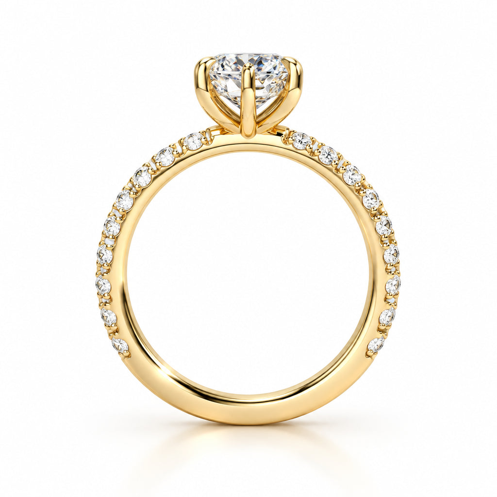 A yellow gold engagement ring featuring a large round brilliant-cut center stone and a pavé band with small accent stones, shown on a light beige background.