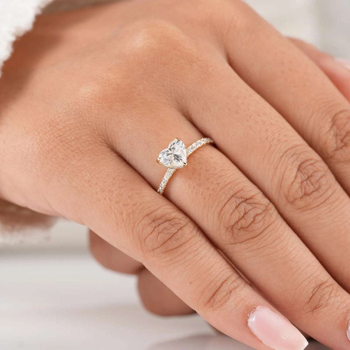 A close-up of a hand wearing a gold ring with a heart-shaped clear gemstone and a pavé band.