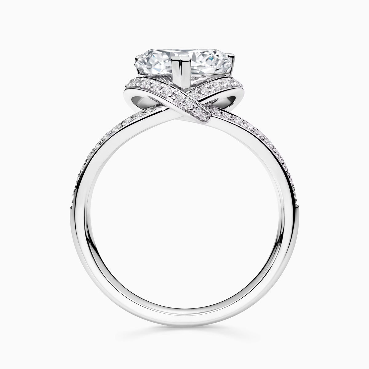 A silver-toned engagement ring featuring a large round brilliant-cut center stone and a crossed band pavé-set with small clear stones, shown on a light gray background.